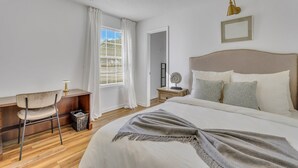 A bedroom with a bed, bedside table, chair, and a window with curtains.