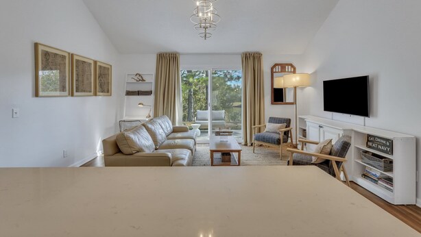 A spacious living room with a large sofa, a coffee table, and a TV mounted on the wall. There is a bookshelf with a sign that reads "Eat, Drink & Beat Navy."