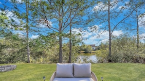 A wicker outdoor sofa with cushions, positioned on a concrete patio with a stone wall and a grassy lawn.