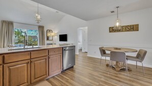 A modern kitchen with wooden cabinets, a stainless steel dishwasher, and a dining area with a round table and chairs.