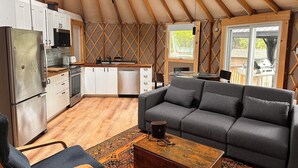 A compact, open-plan living space with a kitchenette, a sofa, a coffee table, and a view of the outdoors. - Yurtopia on the Lake (Lanark Highlands)