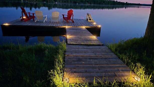 A wooden dock extending into calm water, with chairs and a small table, surrounded by grass. - Yurtopia on the Lake (Lanark Highlands)
