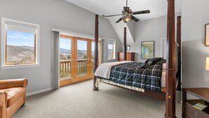 Une chambre à coucher avec un lit à baldaquin, un ventilateur de plafond et une vue sur l’extérieur grâce à de grandes fenêtres.