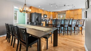 Une cuisine moderne avec des meubles en bois, un grand îlot central et un coin repas comprenant une longue table et des chaises.
