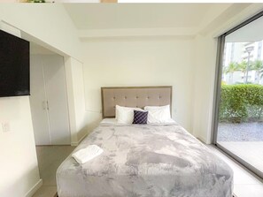 A bedroom with a bed, a television mounted on the wall, and a large window. - Azure Aruba-3BR Resort Style Villa by Eagle Beach (Oranjestad)