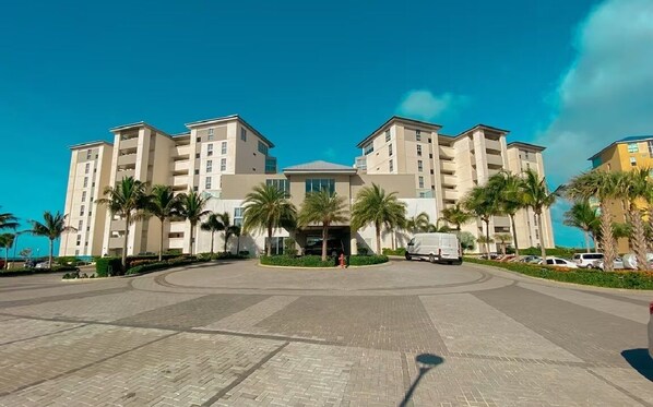 A multi-story hotel with a central courtyard, palm trees, and a clear blue sky. - Azure Aruba-3BR Resort Style Villa by Eagle Beach (Oranjestad)