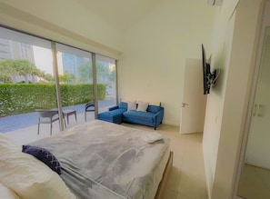 A bedroom with a bed, a blue sofa, a TV mounted on the wall, and a sliding glass door leading to an outdoor area. - Azure Aruba-3BR Resort Style Villa by Eagle Beach (Oranjestad)