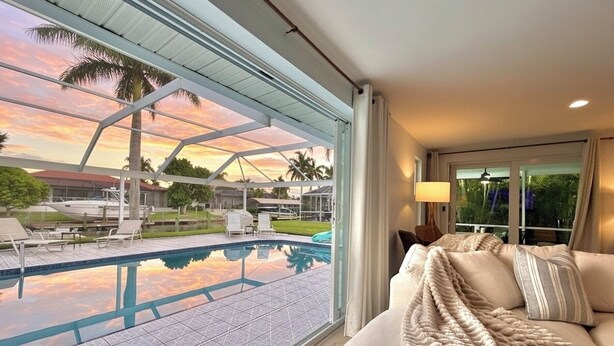 A room with a large window overlooking a swimming pool and a sunset view. - Beautiful Gulf Access Home with Heated Pool and Private Dock in Yacht Club (Cape Coral)