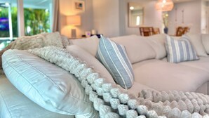 A modern living room with a white sofa, striped pillows, and a fluffy throw. - Beautiful Gulf Access Home with Heated Pool and Private Dock in Yacht Club (Cape Coral)