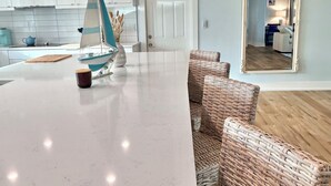 A modern kitchen with white cabinets, a white marble countertop, and a sailboat decoration. There are wicker chairs around the counter and a large mirror on the wall. - Beautiful Gulf Access Home with Heated Pool and Private Dock in Yacht Club (Cape Coral)