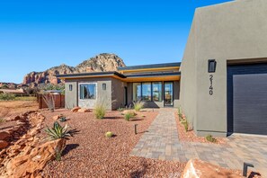 A modern house with a stone facade, a paved driveway, and a mountain backdrop. - Mystic Mesa | Heated Pool, Spa, Firepit, Views (Sedona)