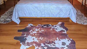 A bedroom with a stone-textured wall, two bedside lamps, a bed with a light blue bedspread, and a large animal hide rug on the floor.
