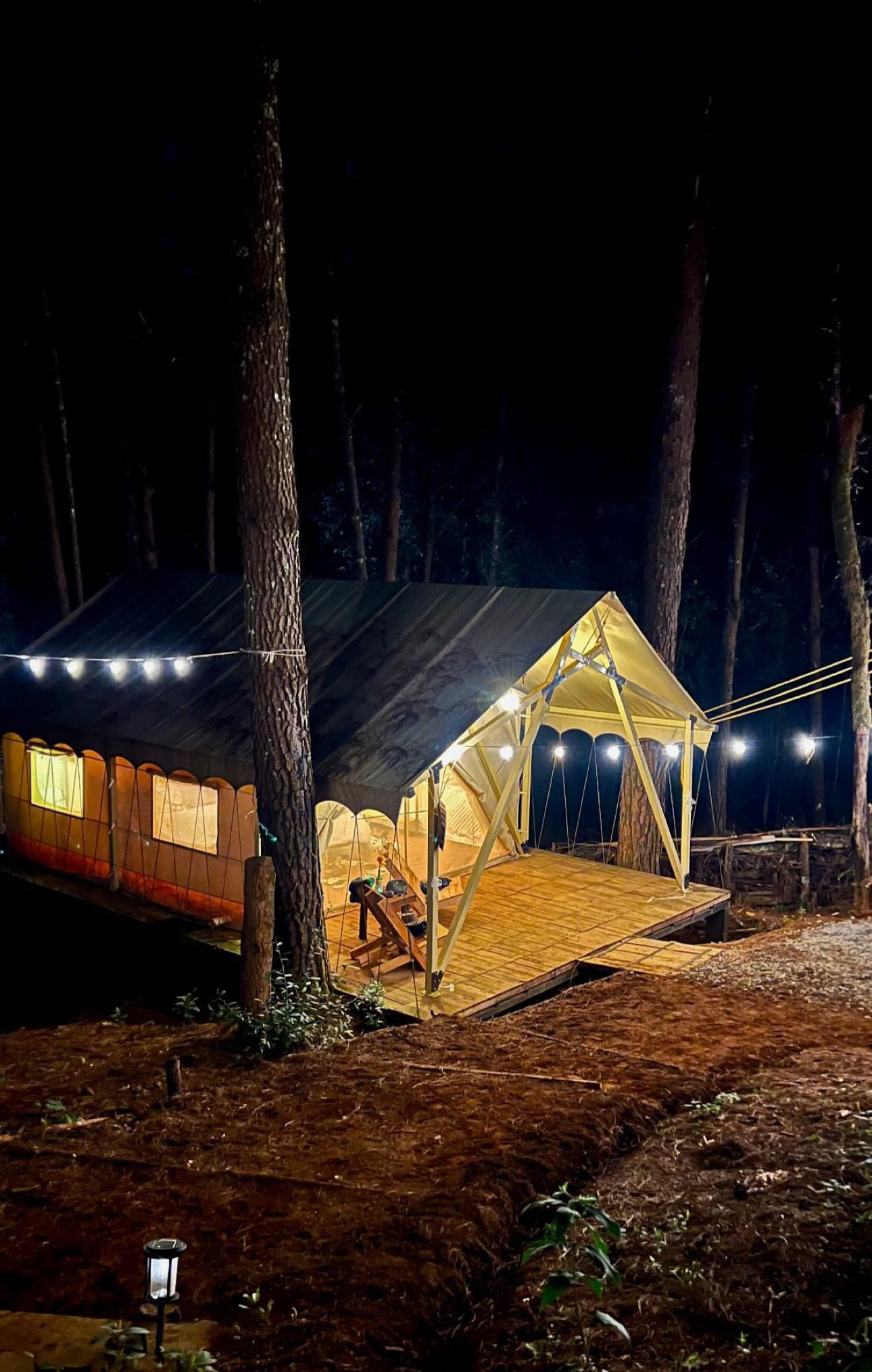 Campa con carpas de noche con luces colgantes, una terraza de madera y un farol.