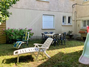Une terrasse avec une table et des chaises, une chaise longue et un pot de fleurs.