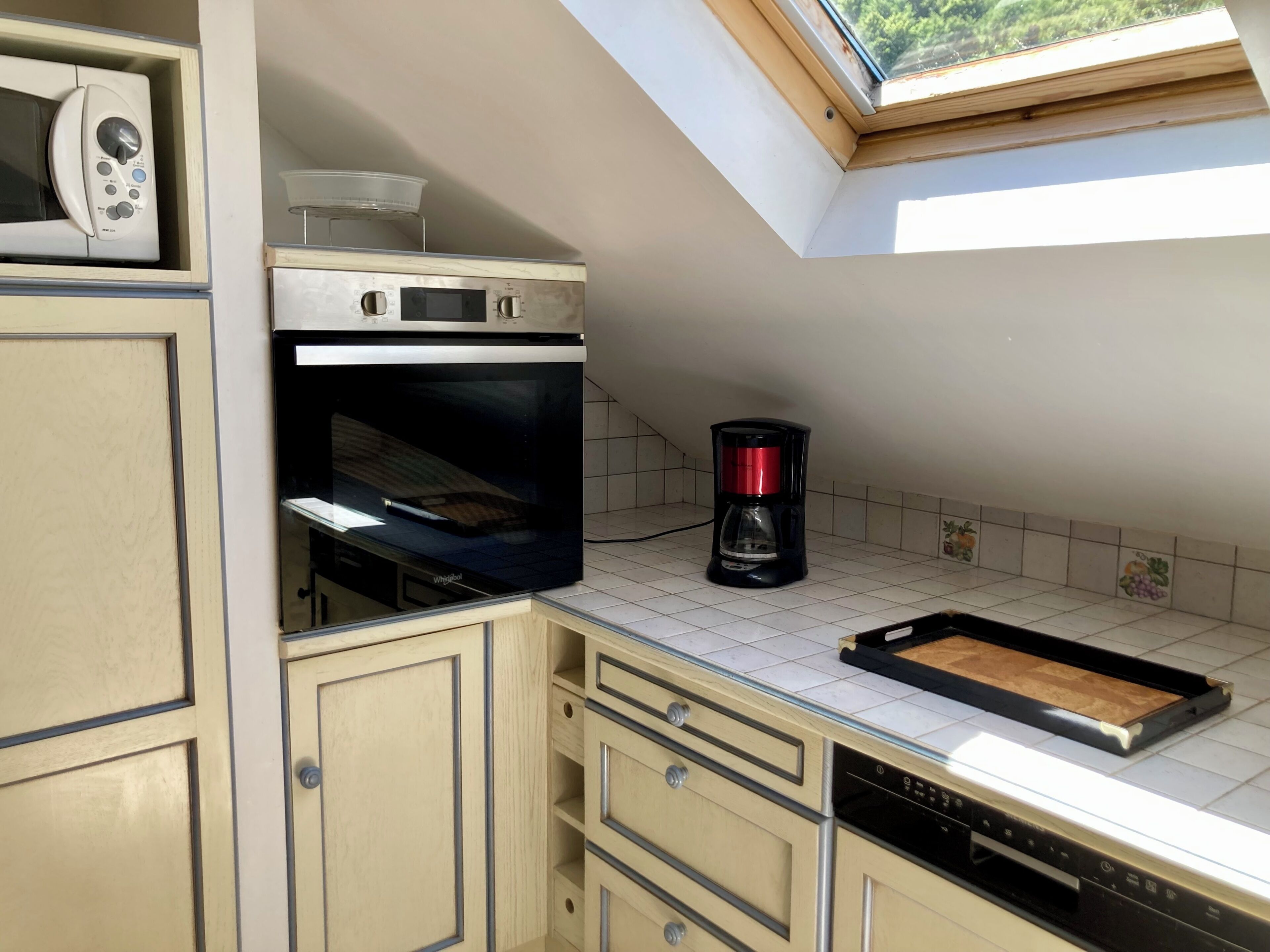 A kitchen with a microwave, oven, coffee maker, and a skylight.