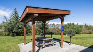 A wooden pavilion with a picnic table, surrounded by grass and trees, under a clear sky. - Aspen Suites Hotel Fairbanks (Fairbanks)