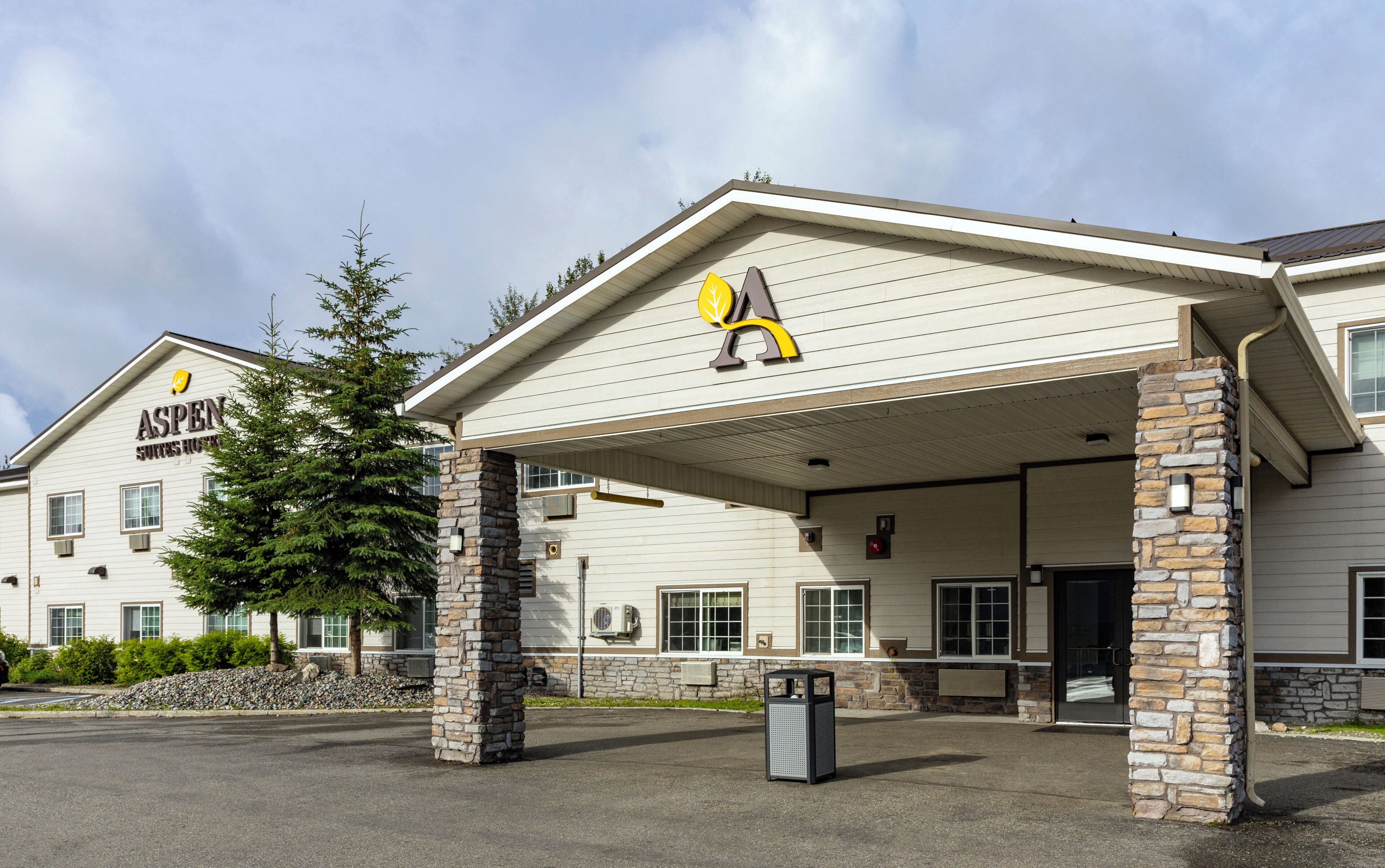 A hotel with a covered entrance, stone pillars, and a sign for Aspen Suites Hotel.