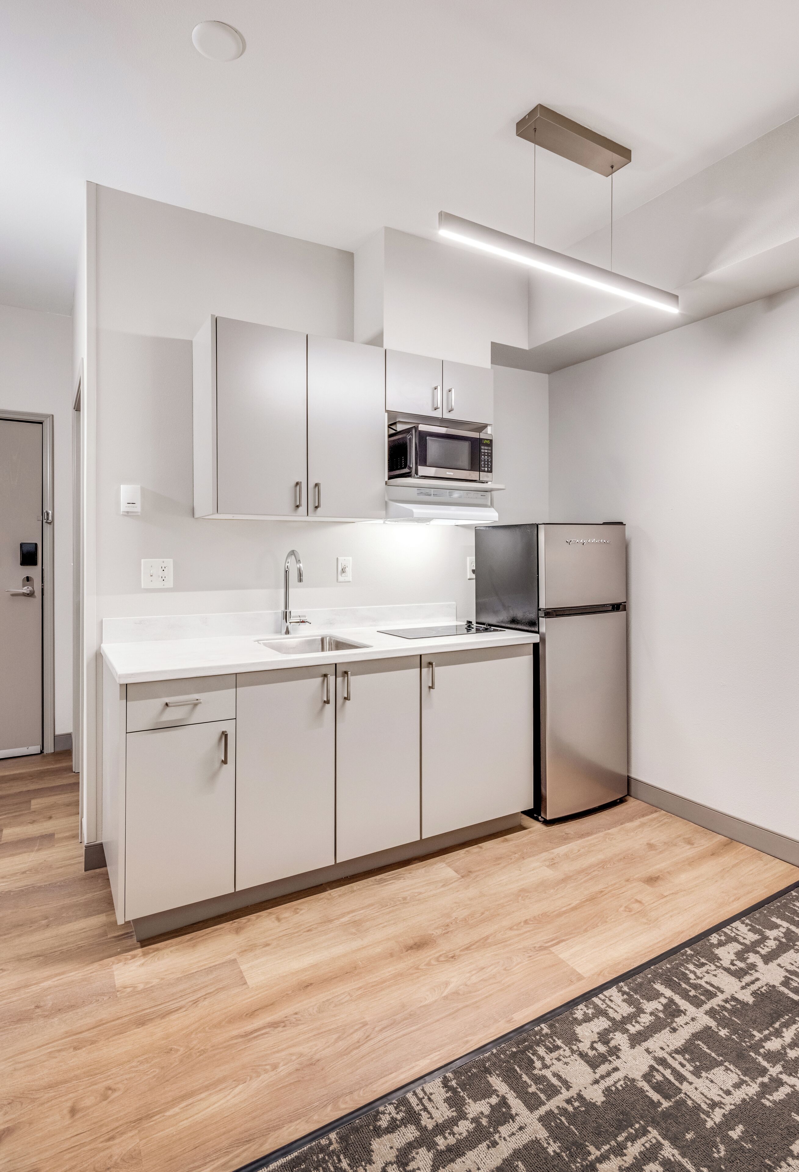 A modern kitchen with white cabinetry, a stainless steel refrigerator, and a microwave.