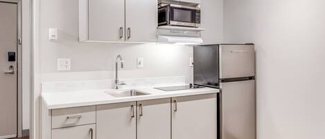 A modern kitchen with white cabinetry, a stainless steel refrigerator, and a microwave.