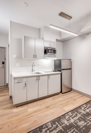 A modern kitchen with white cabinetry, a stainless steel refrigerator, and a microwave. - Aspen Suites Hotel Fairbanks (Fairbanks)