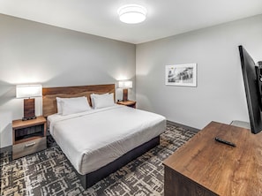 Una camera d'albergo con un letto, due lampade sui comodini, una TV, una scrivania e un tappeto decorato.