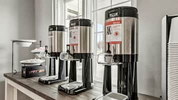 A coffee station with four coffee machines, each with a stainless steel body and a glass carafe.