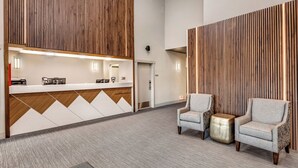 A reception area with a wooden panel wall, a modern chandelier, two armchairs, and a reception desk. - Aspen Suites Hotel Fairbanks (Fairbanks)