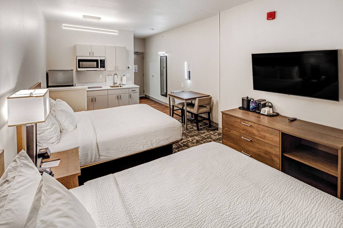 Ein Hotelzimmer mit zwei Betten, einem Schreibtisch, einer Mikrowelle, einem Kühlschrank, einem Fernseher und einer Kaffeemaschine.