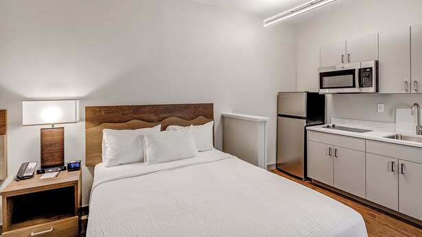 A hotel room with a bed, bedside table with a lamp, a microwave, and a small kitchenette. - Aspen Suites Hotel Fairbanks (Fairbanks)