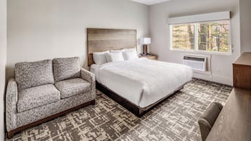 A hotel room with a bed, a sofa, a desk, a window, and a ceiling light.