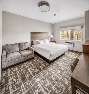 A hotel room with a bed, a sofa, a desk, a window, and a ceiling light. - Aspen Suites Hotel Fairbanks (Fairbanks)