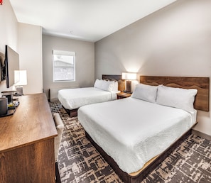 A hotel room with two beds, a desk, a TV, and a window.