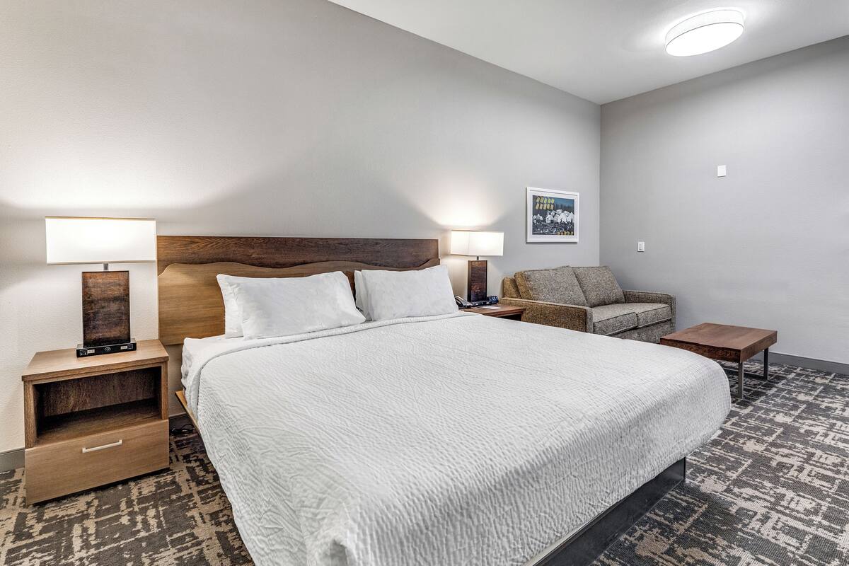 Ein Hotelzimmer mit einem großen Bett, zwei Nachttischen mit Lampen, einem Holzkopfende, einer kleinen Couch und einem gemusterten Teppich.