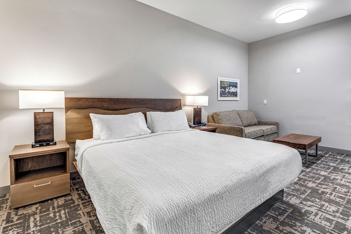 Una camera d'albergo con un letto grande, due comodini con lampade, una testiera in legno, un divano piccolo e un tappeto a motivi.