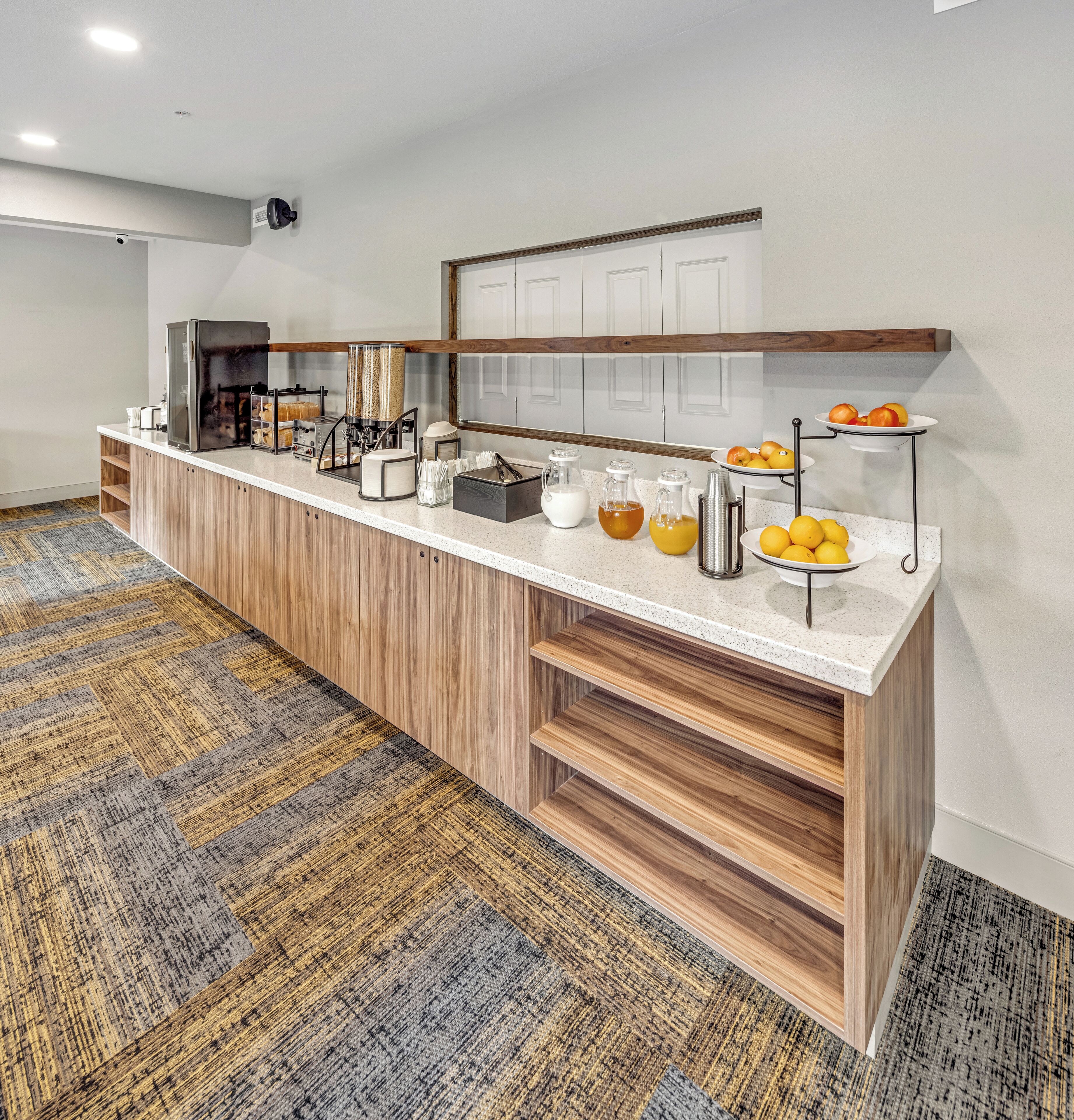 A breakfast bar with a coffee machine, juice dispensers, and a fruit display.