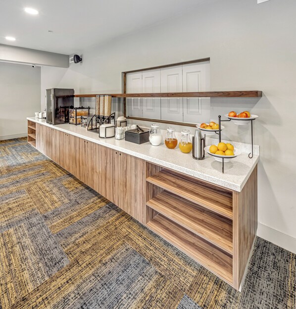 A breakfast bar with a coffee machine, juice dispensers, and a fruit display. - Aspen Suites Hotel Fairbanks (Fairbanks)