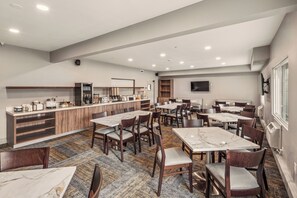 A spacious dining area with multiple tables and chairs, a kitchen area with appliances, and a television mounted on the wall. - Aspen Suites Hotel Fairbanks (Fairbanks)
