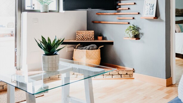 A modern living room with a glass coffee table, a grey accent wall, wooden slats, a flat-screen TV, and a blue sofa.