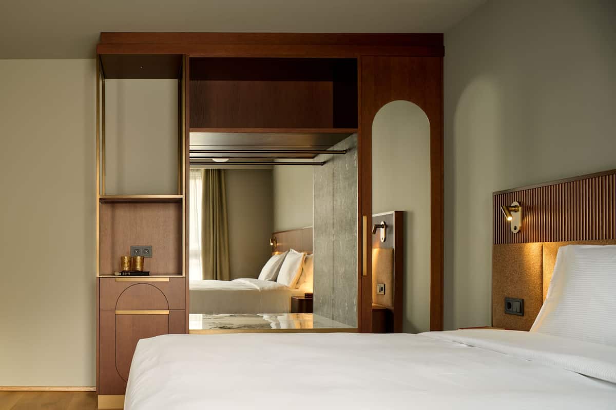A hotel room with a bed, a desk, a wardrobe, and a mirror.