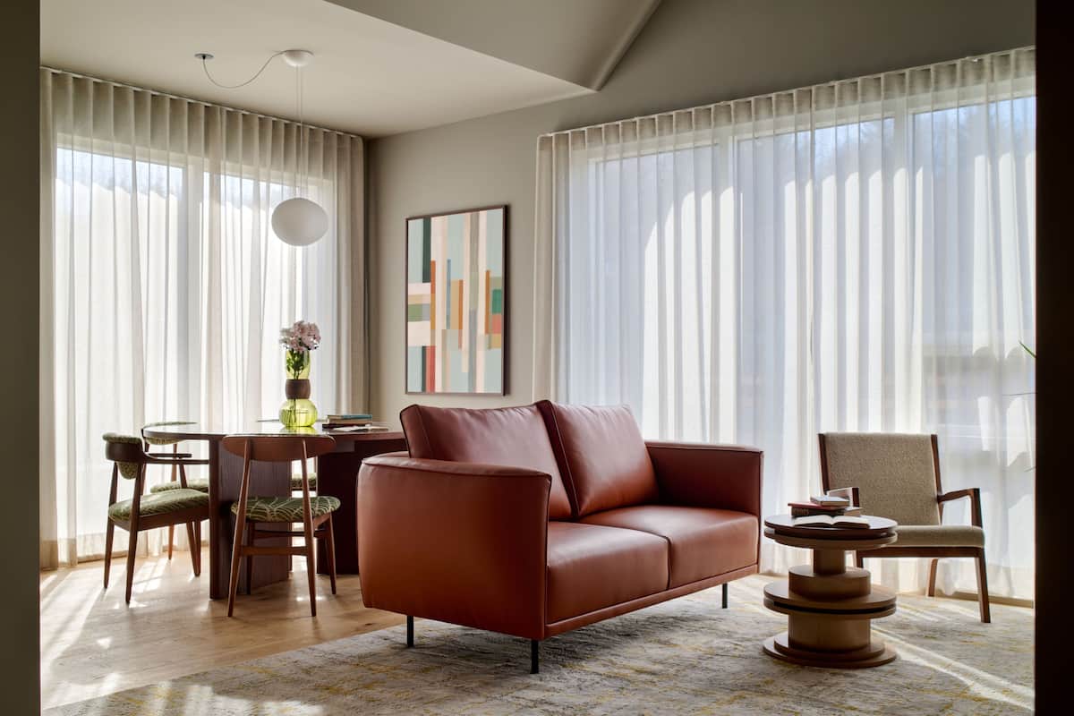 A modern living room with a leather sofa, a dining table with chairs, and a large window with sheer curtains.