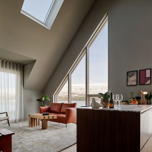 A modern living room with a large window, a brown leather sofa, a wooden coffee table, and a kitchen area with a marble countertop. - Skald Hotel Akureyri, Curio Collection By Hilton (Akureyri)
