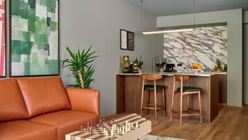A modern living room with a leather sofa, a wooden chess table, and a kitchen area with a marble backsplash.