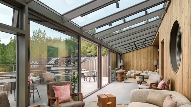 Ein geräumiger Raum mit Glasdecke, Holzwänden und verschiedenen Sitzgelegenheiten, darunter Sofas und Sessel.