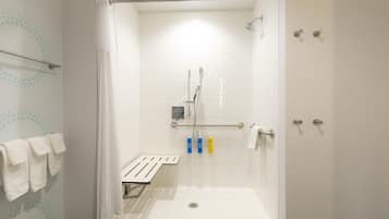 A walk-in shower with white tiled walls, a glass door, and a handrail.