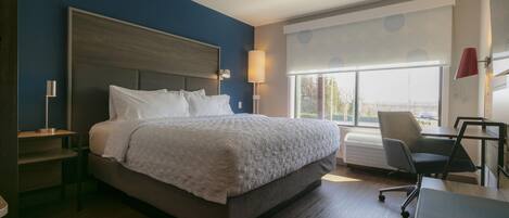 A hotel room with a large bed, a desk, a chair, and a window with blinds.