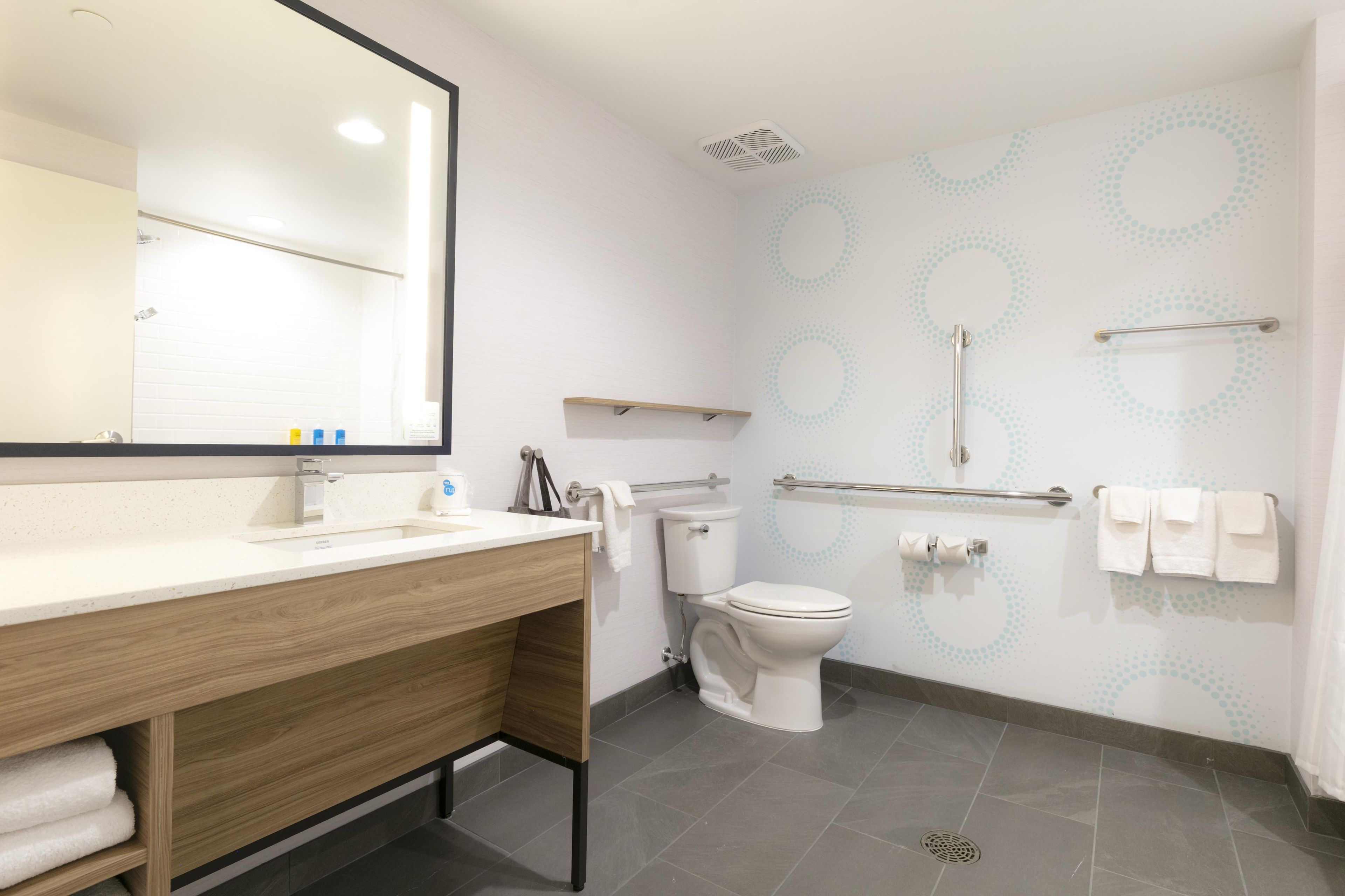 Et moderne badeværelse med et trækommode, toilet, brusebad med gelænder og et spejl.