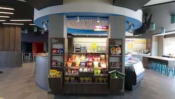 Ein Imbissstand mit verschiedenen verpackten Snacks, einer Kaffeemaschine und einer Sitzgelegenheit mit Hockstühlen.
