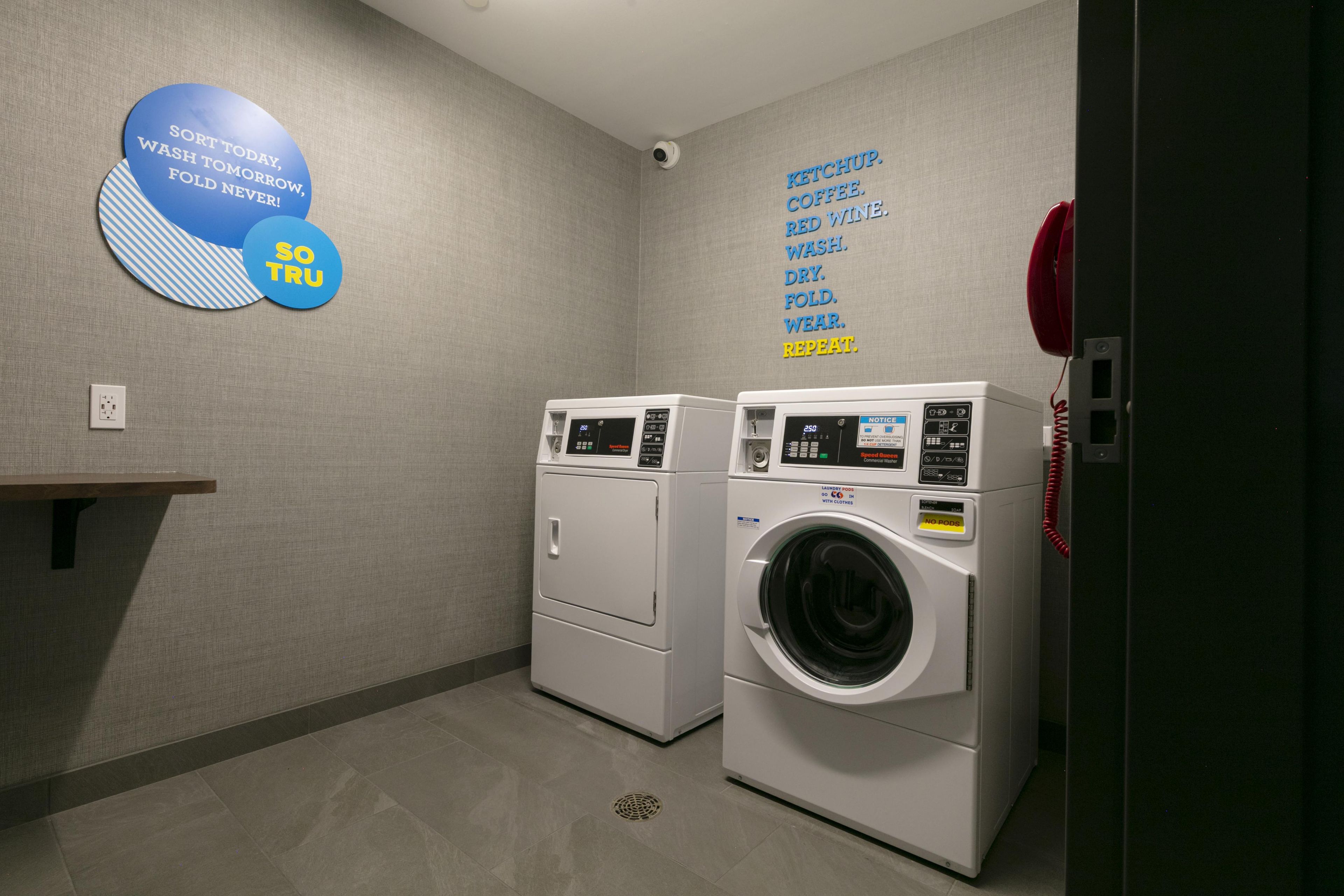 A laundry room with two washing machines, a wall-mounted sign with laundry instructions, and a red telephone.