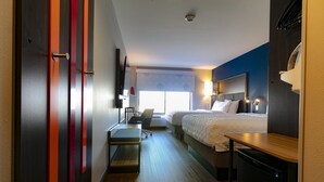 A hotel room with a bed, a desk, a chair, a small refrigerator, and a window with blinds. - Tru By Hilton Hazleton (Hazleton)