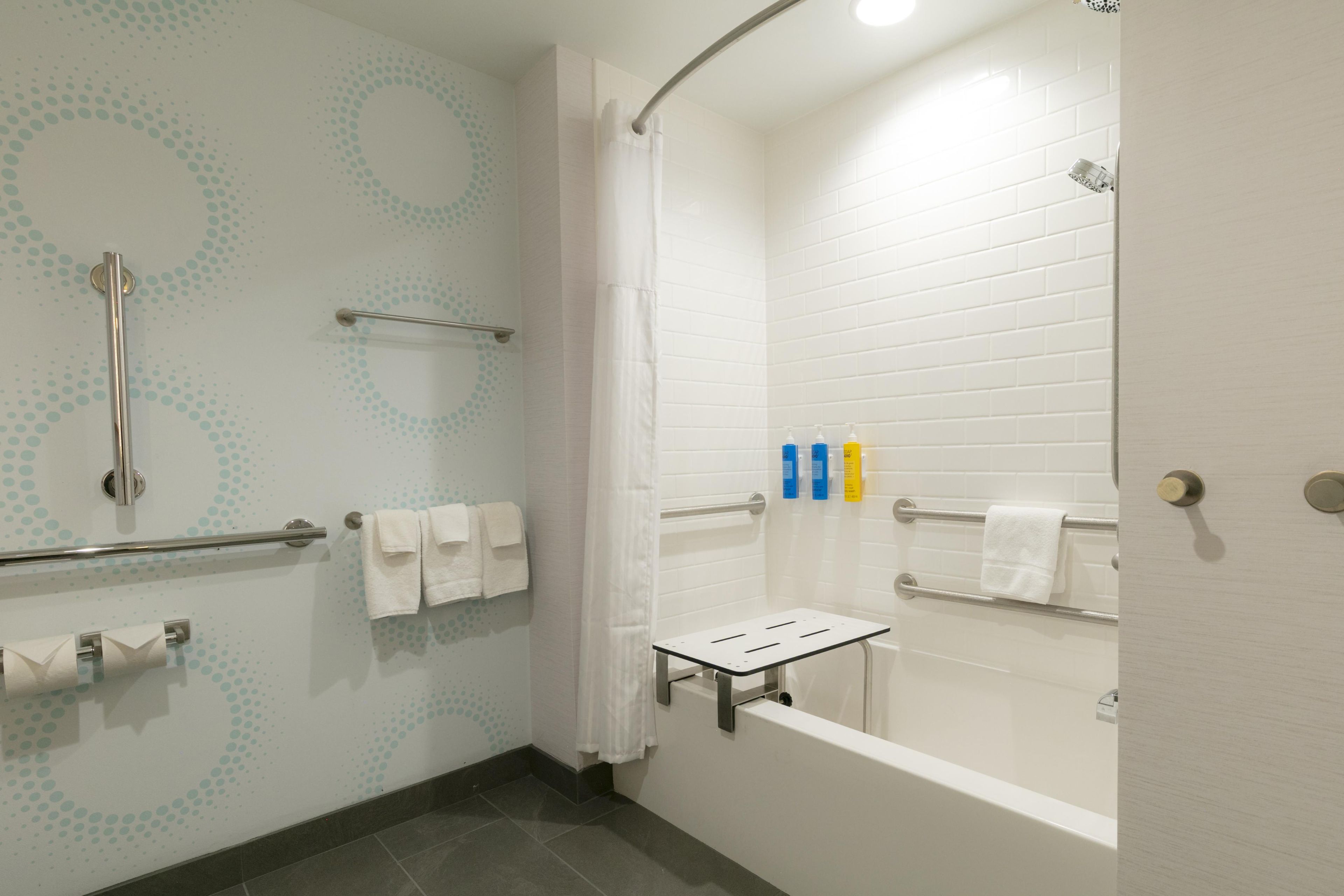 A modern bathroom with a shower, grab bars, a towel rack, and a toilet paper holder.